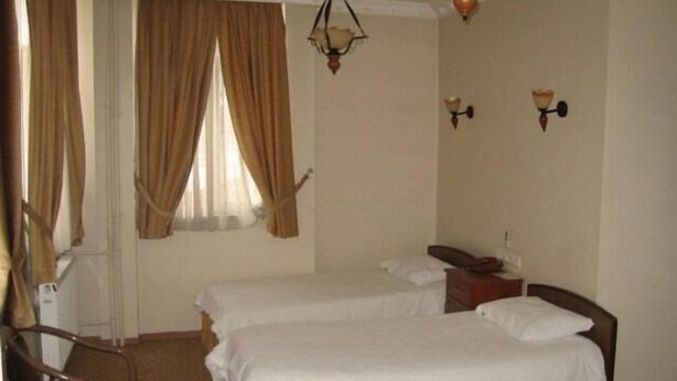 Habitación de hotel con dos camas, una silla, una mesita de noche y una lámpara.