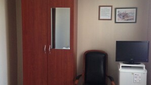 Una habitación con un armario de madera, una butaca de cuero negro, un mueble blanco con televisor y dos cuadros en la pared.