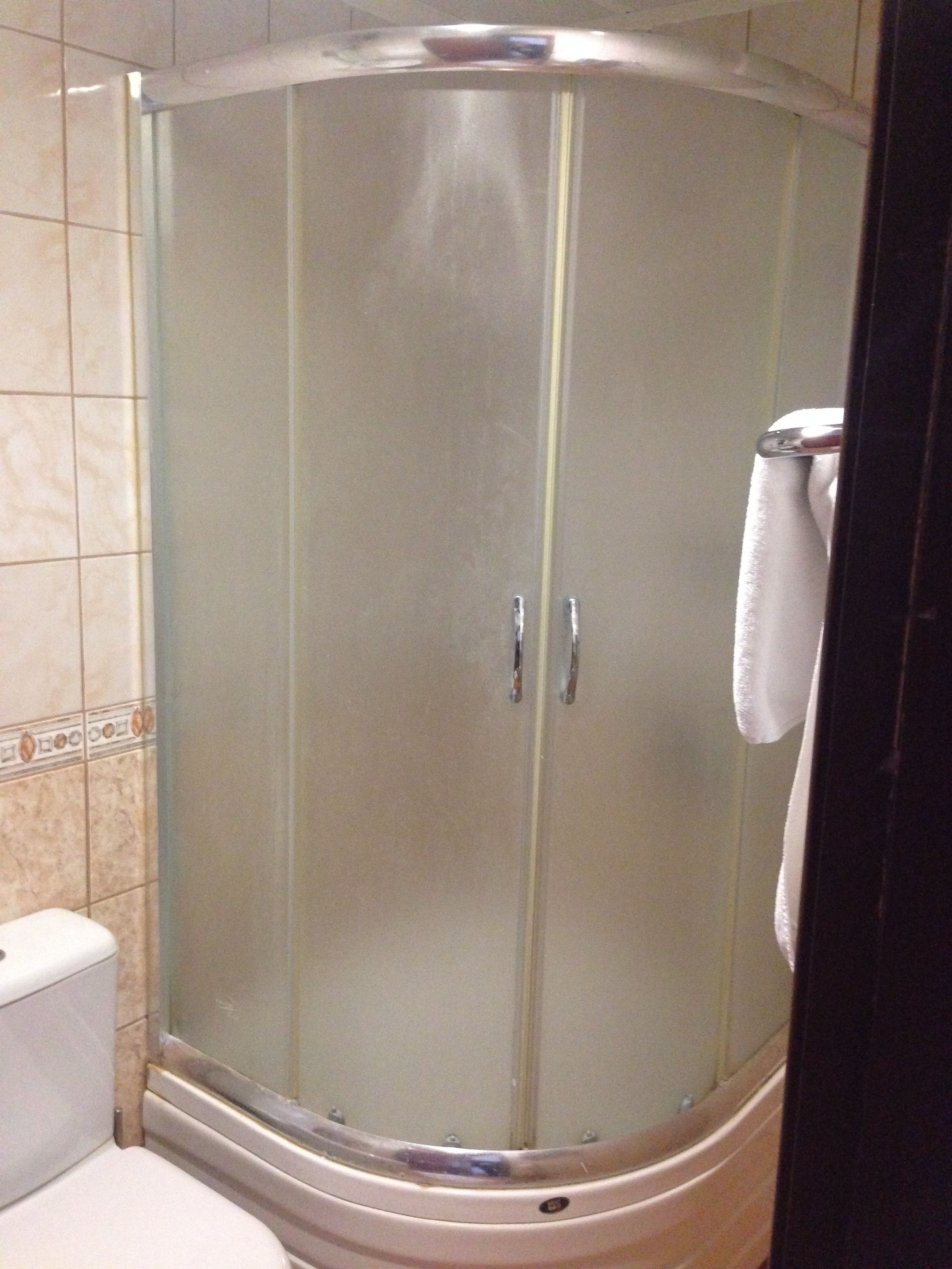 Cabina de ducha con paredes de vidrio y una toalla blanca colgada del pomo de la puerta.