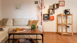 A cozy living room with a sofa, a coffee table with food and a glass of wine, a bookshelf, and a coffee machine.