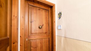 A wooden door with a brass handle, a small wall-mounted light switch, and a decorative wreath on the wall.
