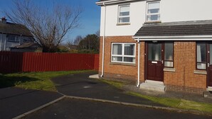 A two-story residential building with a red brick facade, white windows, and a dark roof. - Portrush Getaway – Family-Friendly Home Near Beaches & Town (Portrush)