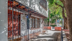 Un estrecho callejón con una reja de metal, un acceso con azulejos y un sendero bordeado de árboles.