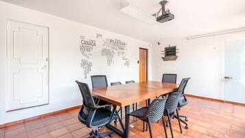 A conference room with a wooden table, black chairs, a whiteboard with country names, and a ceiling fan.