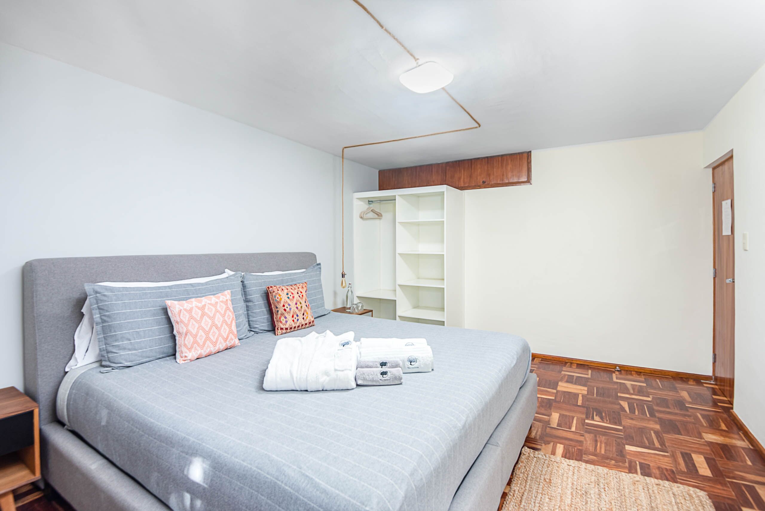 Un dormitorio con cama, mesitas de noche, armario y estante colgante.