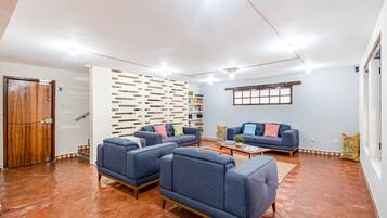A spacious living area with a modern design, featuring a wooden door, a white wall with a decorative panel, and a blue sofa set.