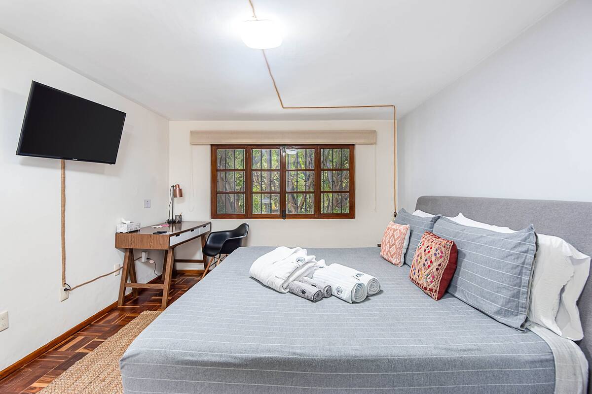 Een slaapkamer met een bed, een bureau, een stoel, een televisie en een raam.
