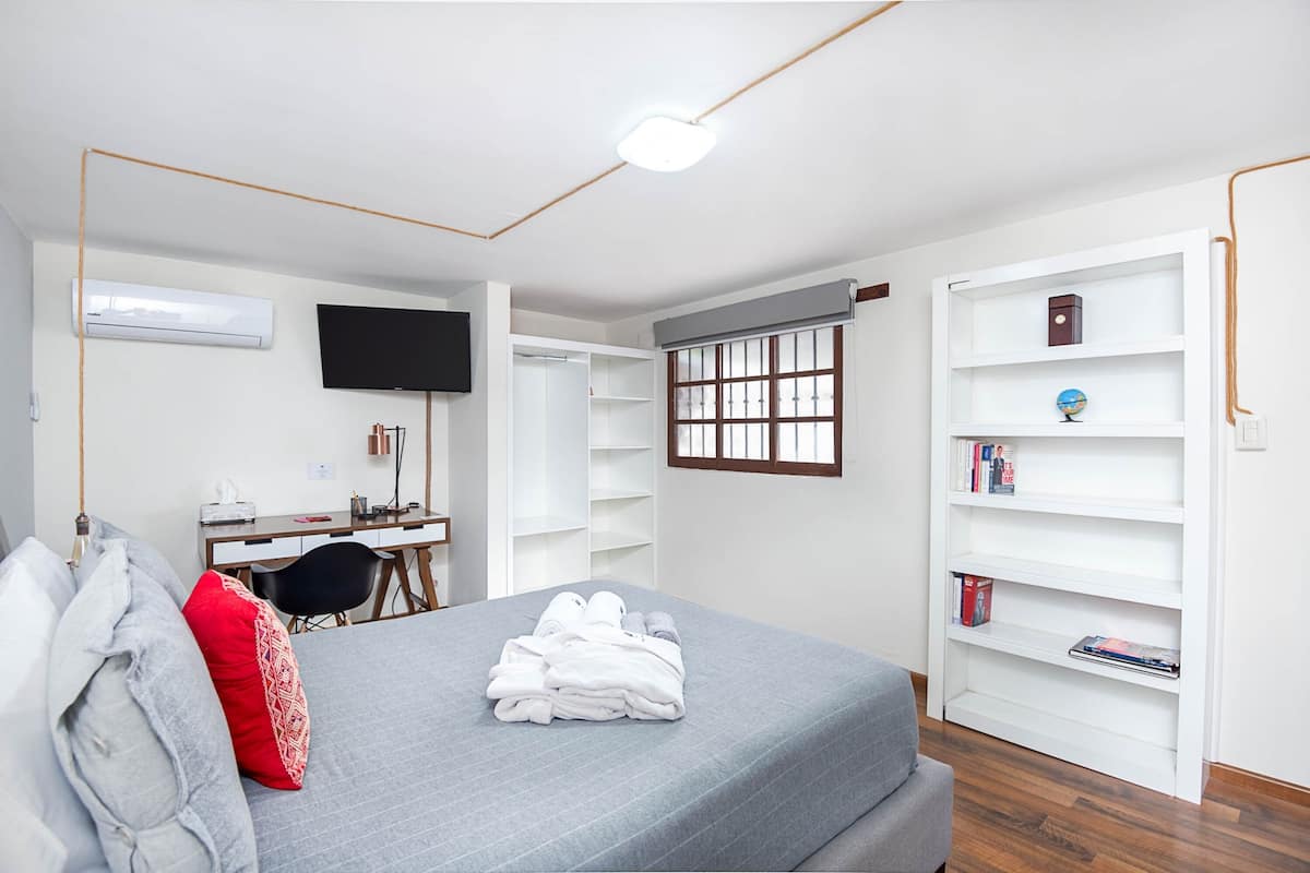 Een slaapkamer met een bed, een bureau, een stoel, een televisie en een boekenkast.