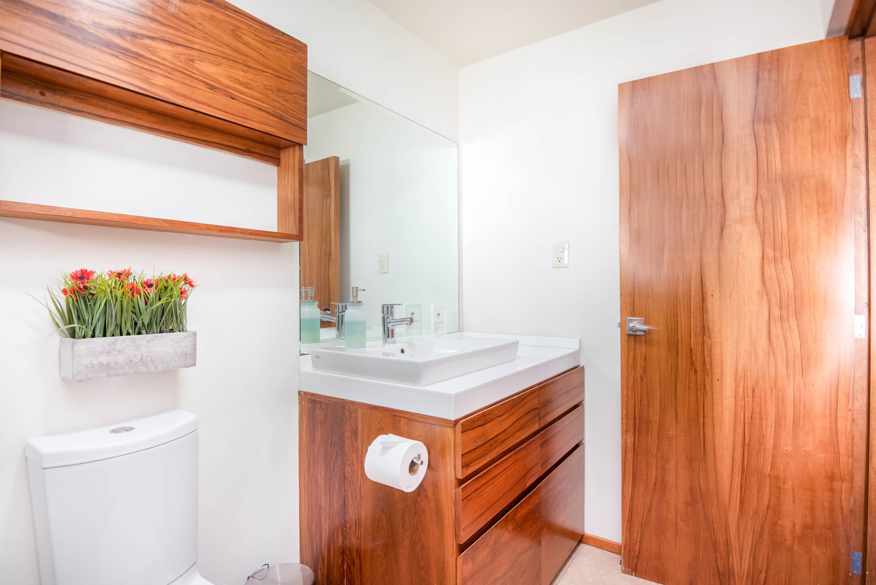 A modern bathroom with a wooden vanity, white sink, and a mirror above it.