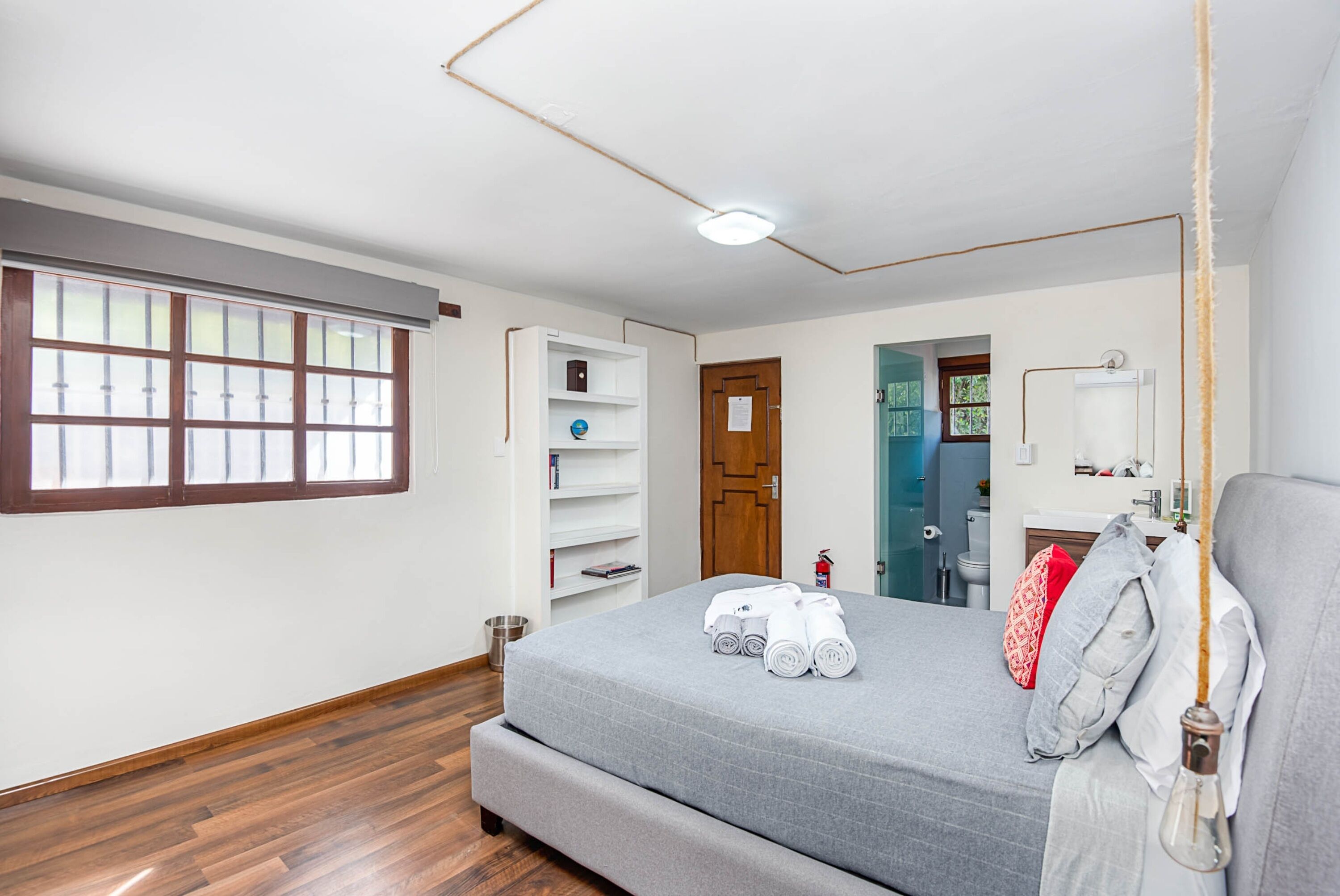 A bedroom with a bed, a wardrobe, a window, and a bathroom visible through an open door.