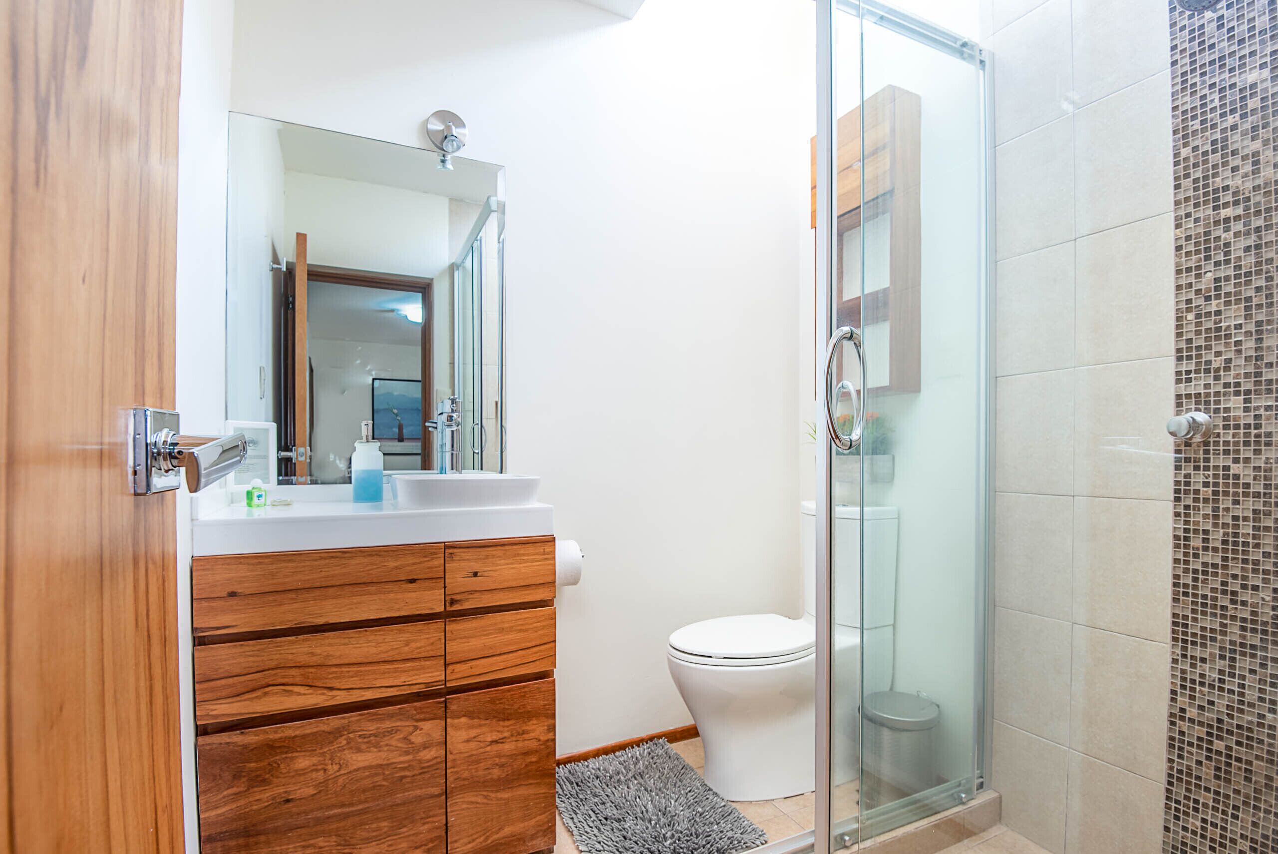 A bathroom with a wooden vanity, a white sink, a mirror, a glass shower enclosure, and a white toilet.