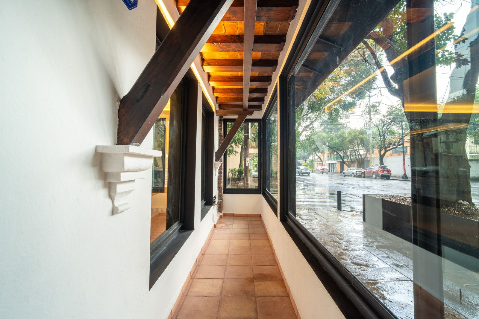 Un pasillo con suelo de baldosas, ventanas amplias y estructura de techo de madera.