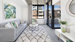 Un salon moderne avec un canapé gris, un tapis à motifs, une table basse et un tableau accroché au mur.