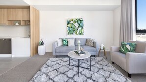 Un salon moderne avec un canapé gris, une table basse ronde et une grande fenêtre avec des rideaux.