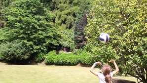 Eine Person spielt mit einem Ball auf einer Wiese, im Hintergrund dichtes Waldgebiet.