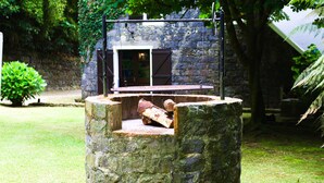Ein steinerner Brunnen mit Metallkonstruktion, umgeben von Grünflächen und einem Steinhaus im Hintergrund.