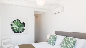 Habitació d'hotel amb un llit, parets blanques, almoina amb dibuixos de fulles verdes, una cadira blanca i una obra d'art de grans dimensions amb un motiu de fulles a la paret.