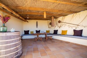 A covered patio with a wooden table, benches, and a seating area with cushions.