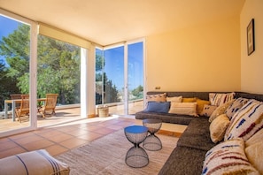 A living room with a sofa, two side tables, a dining area with chairs, and a large sliding glass door leading to an outdoor space.