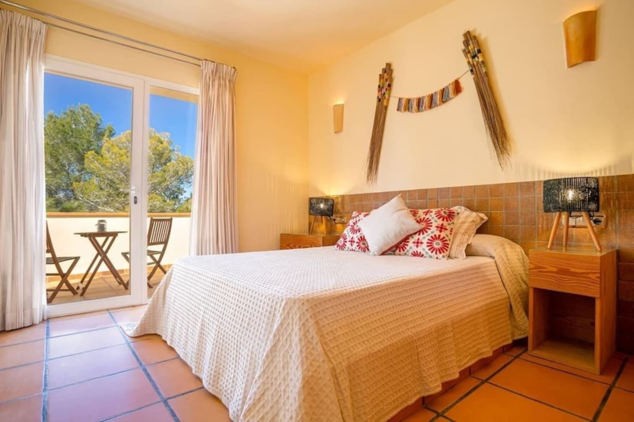Quarto com cama, mesa de cabeceira, luminária, decoração na parede e porta de vidro deslizante para área externa.