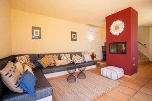 A living room with a sofa, two side tables, a red accent wall, and a staircase.