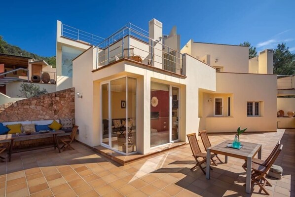 A modern villa with a glass-enclosed patio, a dining area, and a stone wall.