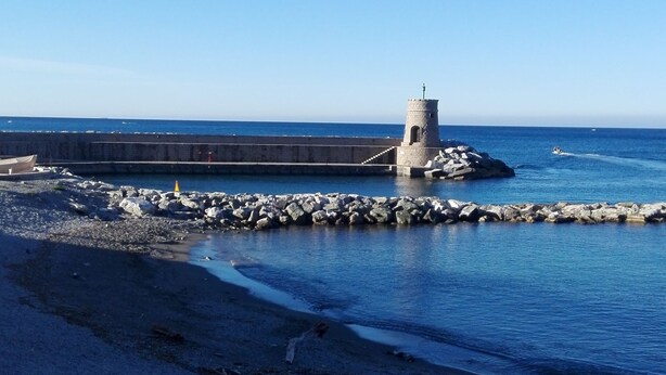 A coastal view with a lighthouse, rocky shoreline, and calm sea.