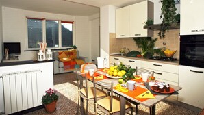 A modern kitchen with white cabinets, a dining table set with orange placemats, and a variety of fruits and vegetables on the counter.