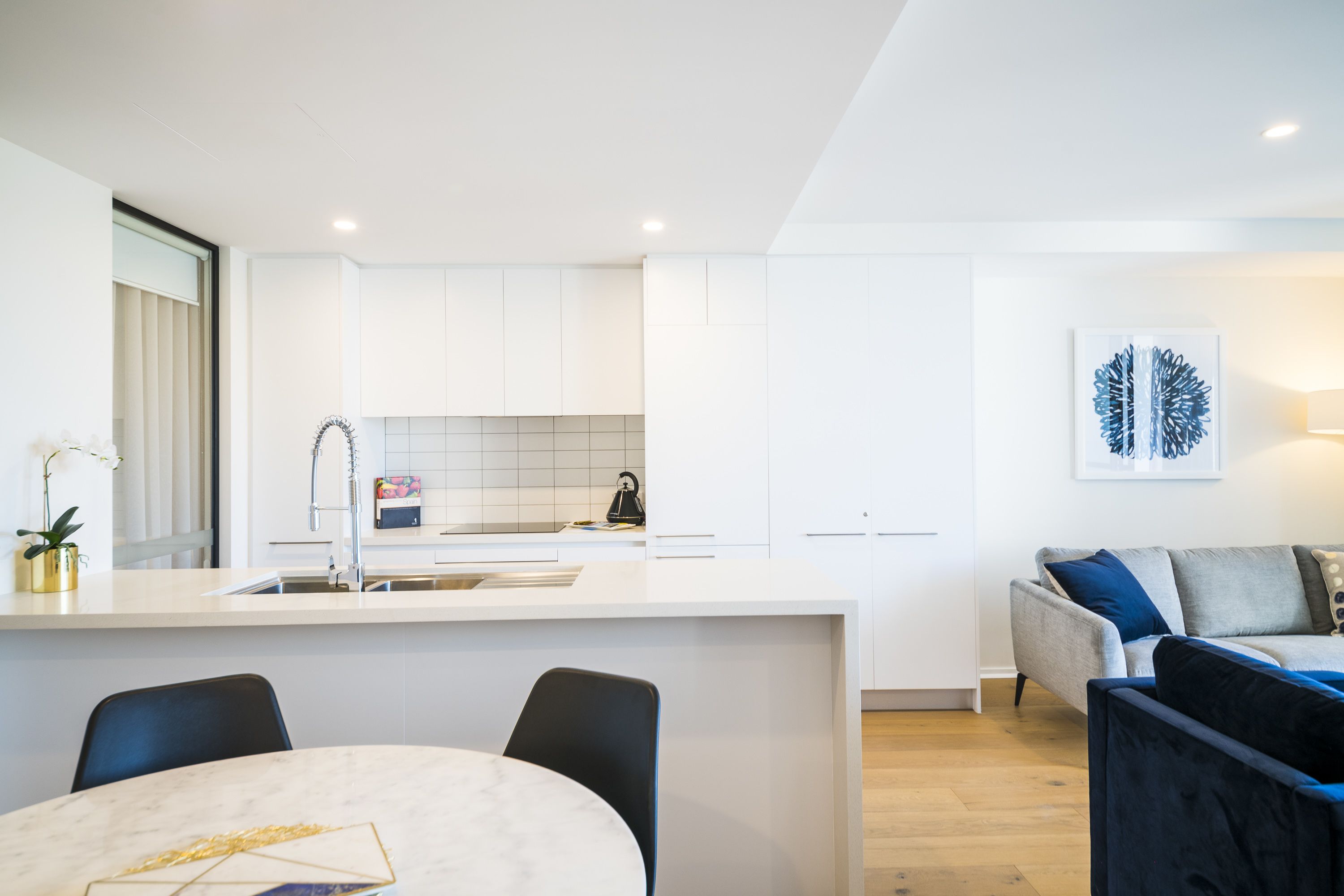 A modern kitchen with white cabinets, a central island, and a dining area with a table and chairs.