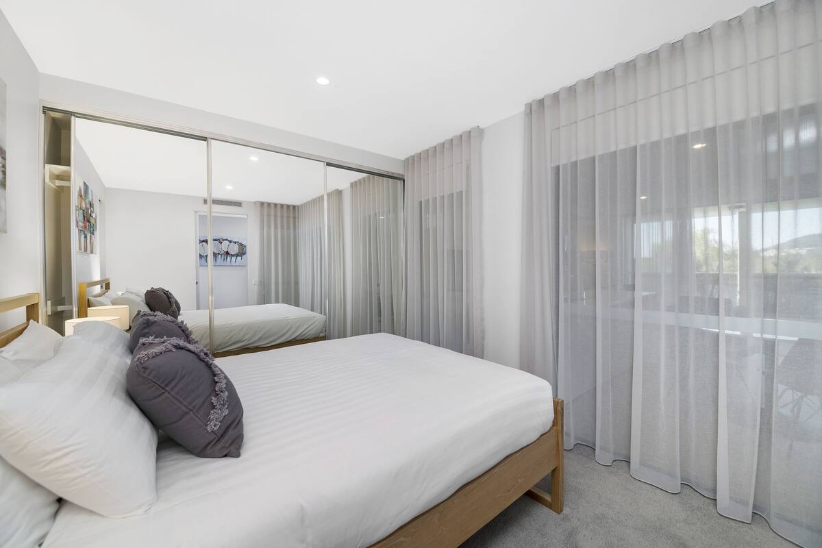 A modern hotel room with a large bed, a sliding glass door, and a view of the outdoors.