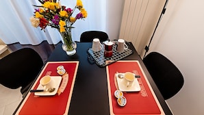 Une table à manger dressée avec deux sets de table, un vase rempli de fleurs et un plateau sur lequel sont empilées des assiettes et des tasses.