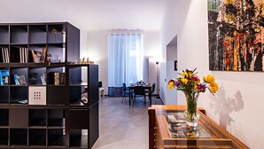 Un salon moderne avec une bibliothèque sombre, un coin repas comprenant une table et des chaises, et un grand tableau abstrait accroché au mur.
