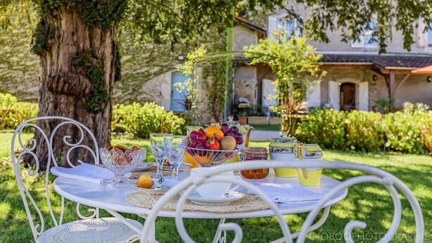 A table set outdoors with a variety of fruits, glasses, and a basket of bread. - GUEST HOUSE OSTAL CASSINIA  (Cassagne)
