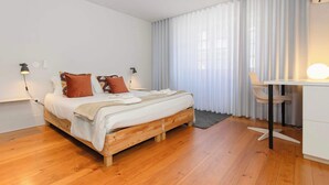 A modern bedroom with a wooden bed, white walls, and a desk with a chair. - Santa Catarina Lively Apartment by Liiiving (Porto)