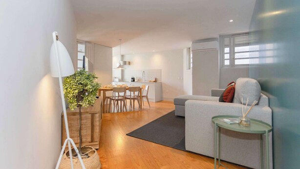 A modern living room with a sofa, a small table, a dining area with chairs, and a kitchen in the background. - Santa Catarina Lively Apartment by Liiiving (Porto)