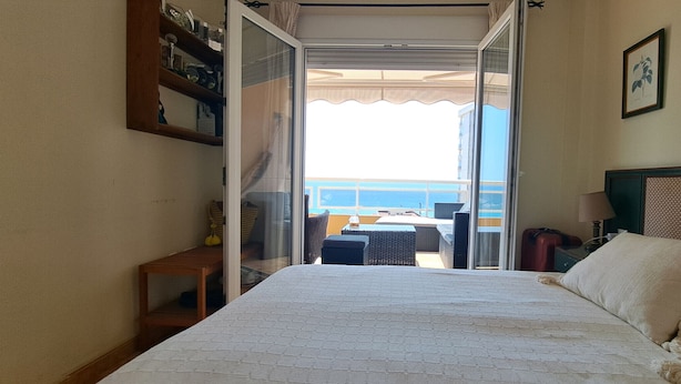Habitación de hotel con cama, una mesita y vista al mar desde una puerta abierta.