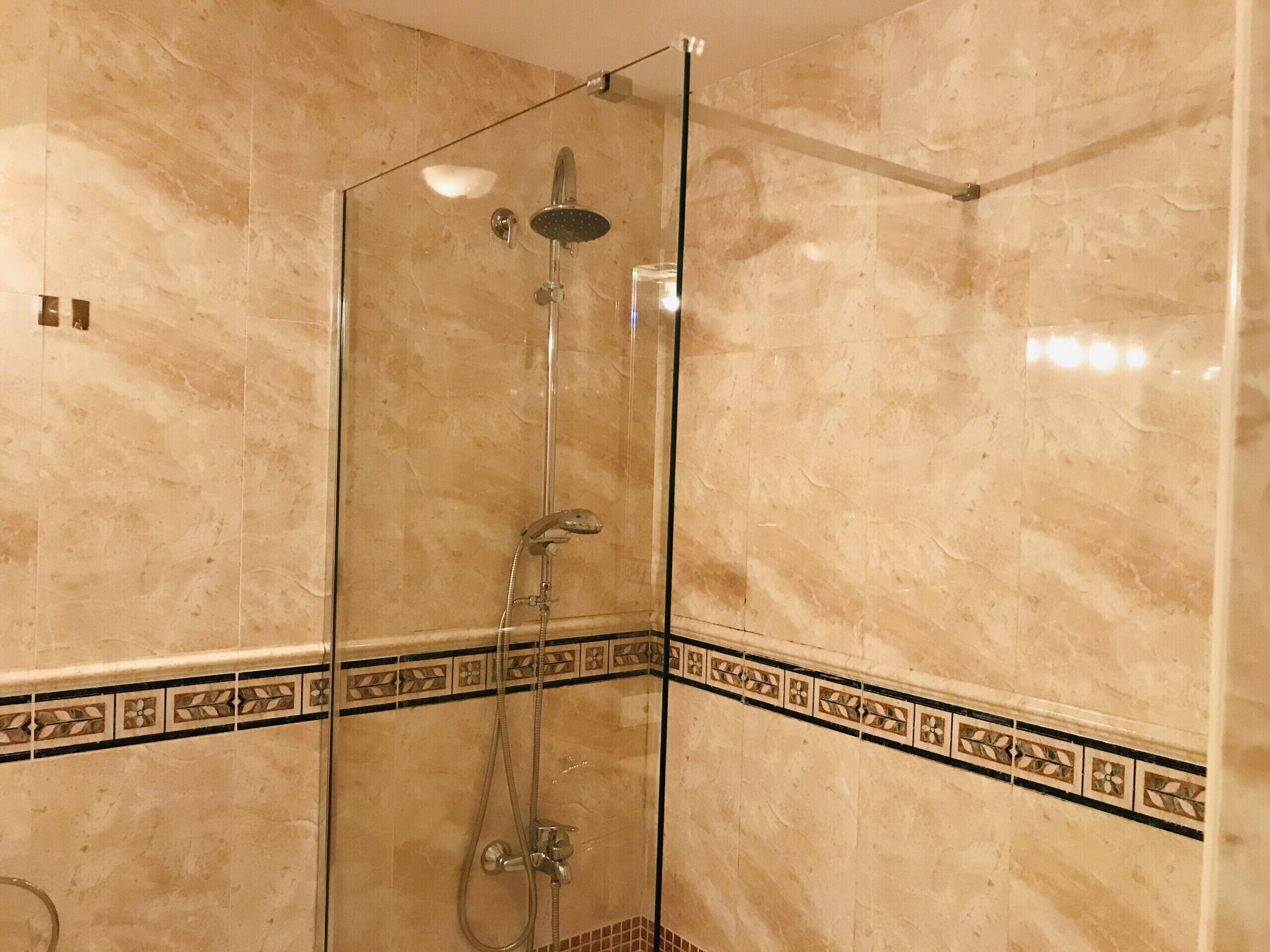 A glass-enclosed shower with a handheld showerhead and a wall-mounted faucet.