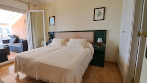 Un dormitorio con una cama grande, una mesita de noche con lámpara, una silla y vistas al balcón exterior.