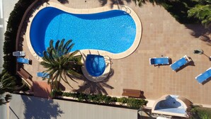 Una piscina grande y ovalada con un jacuzzi, rodeada de sillas de descanso y palmeras.