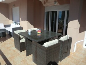 An outdoor patio with a glass-top table, wicker chairs, and a sliding glass door. - A11 EDIFICIO OASIS 8D (Calpe)