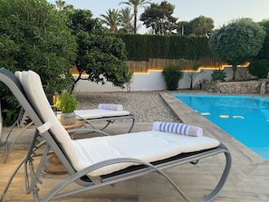 A poolside area with two lounge chairs, a wooden deck, and a pool.