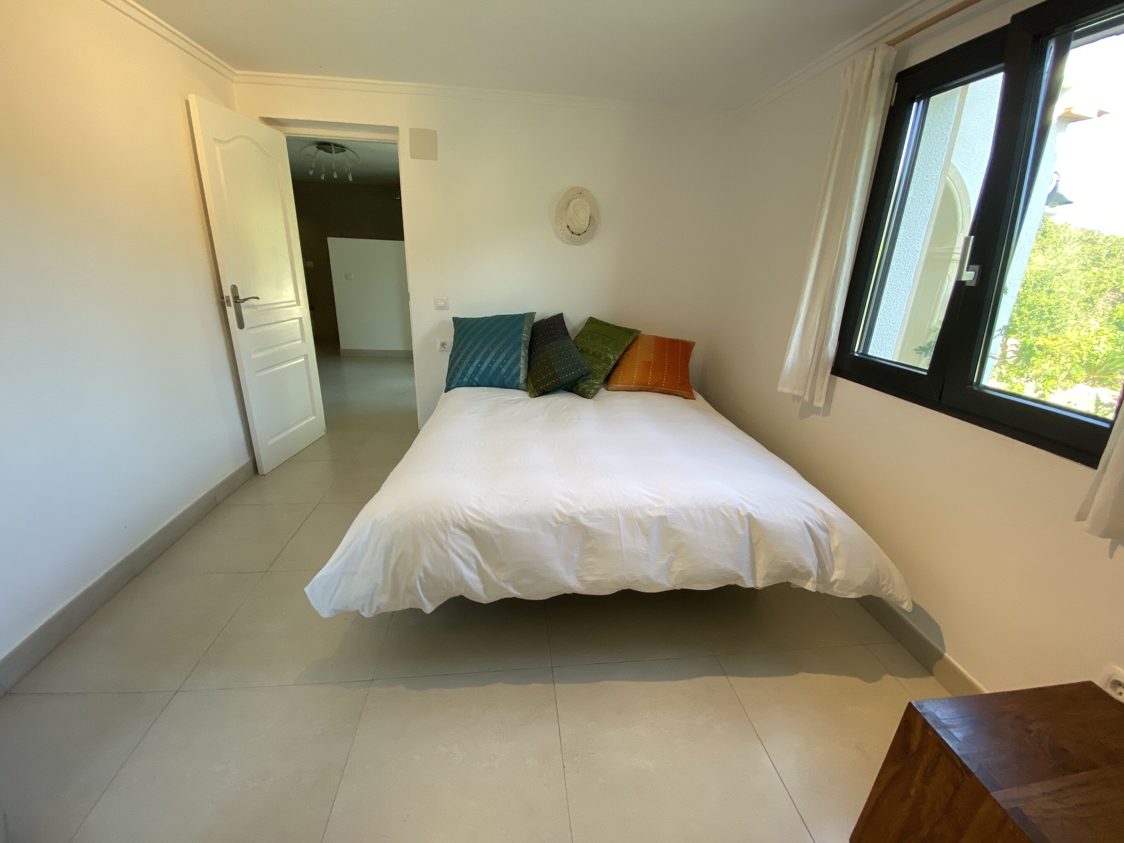 A bedroom with a bed, a window, and a door leading to another room.