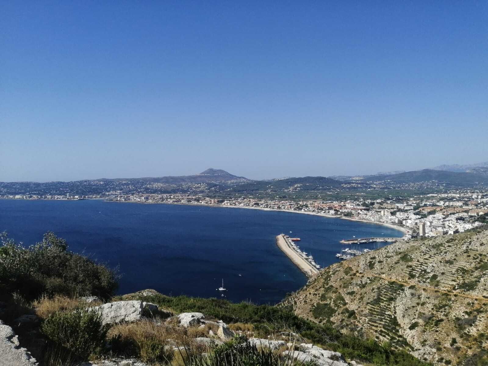 A coastal city with a prominent beach, rocky terrain, and a distant mountain.