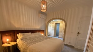 Un dormitorio con una cama grande, una mesita de noche con lámpara, un arco en el acceso y un armario.