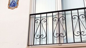 Un edificio con balcón que presenta barandillas de metal negro ornamentado y una ventana con persianas blancas.