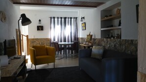 Una sala de estar con un sofá, un sillón amarillo, una mesa de comedor con sillas y una pared de piedra decorativa.