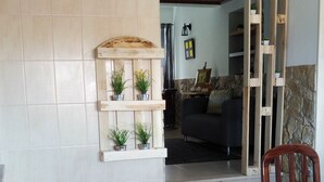 Un comedor con mesa y sillas de madera, suelo de baldosas y estantería empotrada con plantas en macetas.