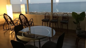 Un coin repas avec une table et des chaises en verre, offrant une vue sur la plage et l’océan.