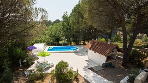 Piscina cercada por árvores, área coberta com teto e mobiliário de exterior.