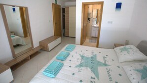 Quarto de hotel com cama, espelho, banheiro e porta que dá para outro cômodo.